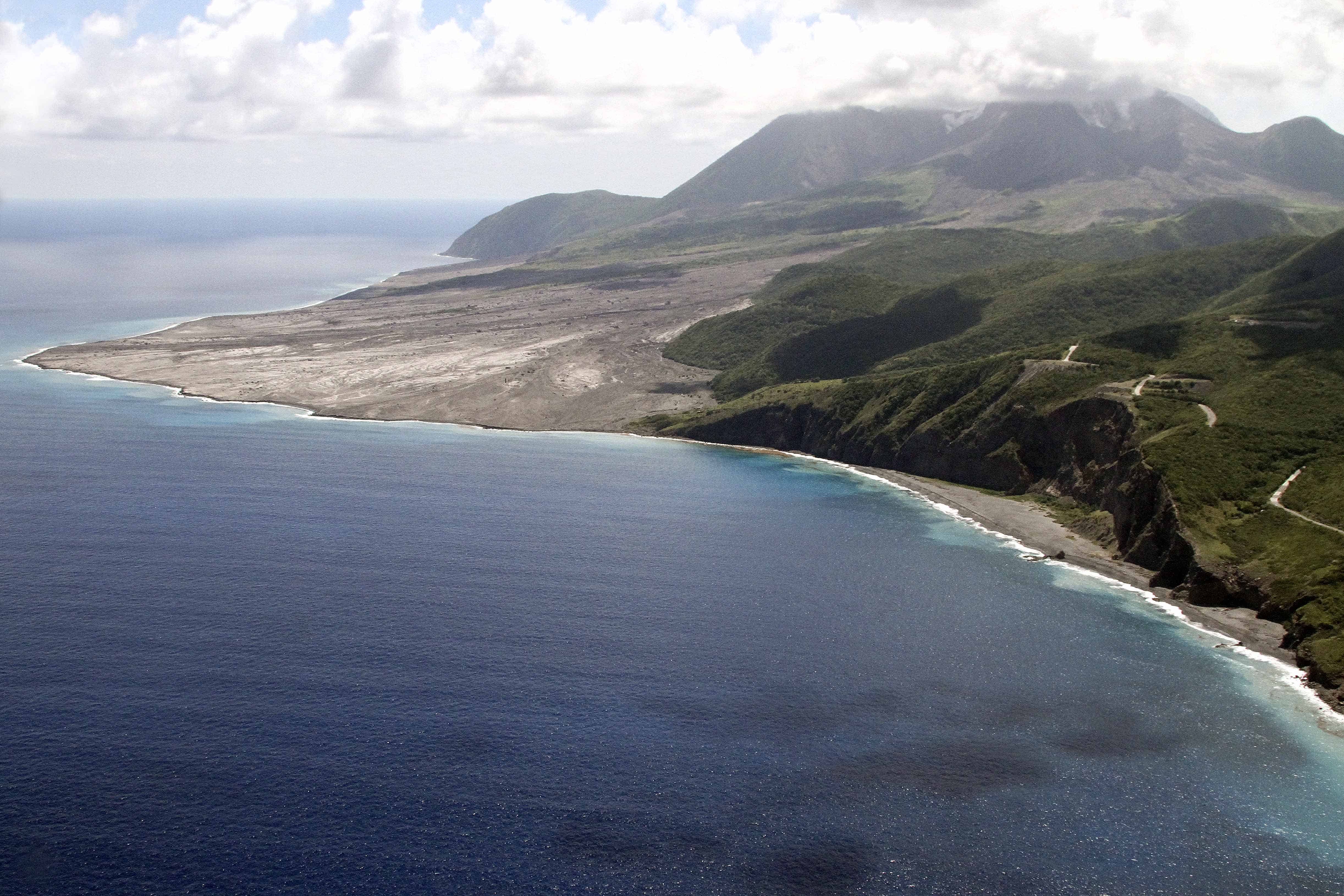 The east coast of Montserrat: in front of the cloud-topped volcano, the volcanic material has covered the former airport and created new land to the east. Copyright: Dr Mike Pienkowski